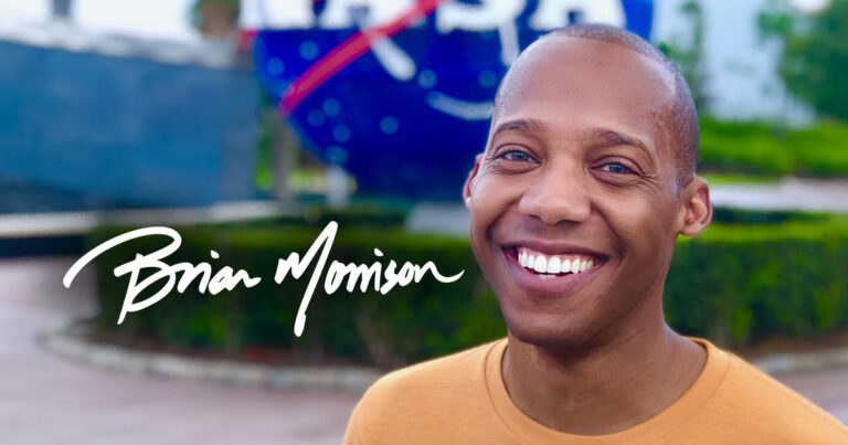 An image of Brian Morrison smiling in front of a NASA sign at the Kennedy Space Center
